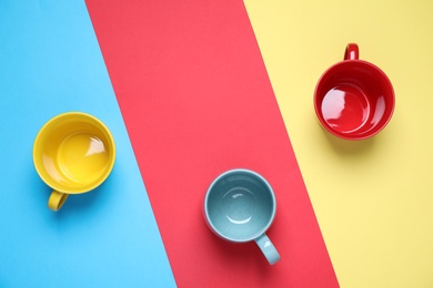 Different bright ceramic cups on color background, flat lay