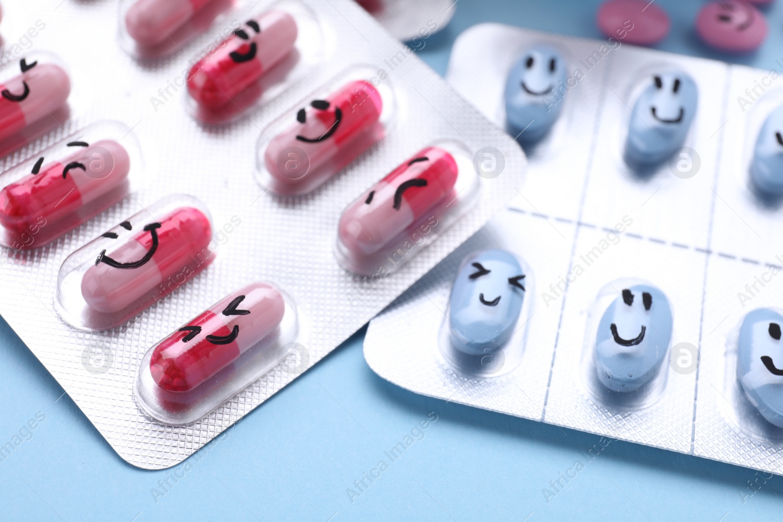 Photo of Blisters of antidepressant pills with emotional faces on light blue background, closeup