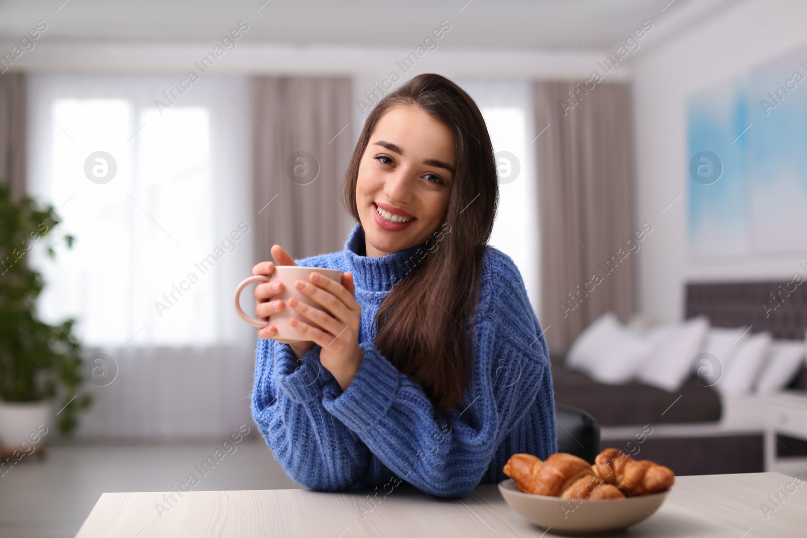 Photo of Young woman drinking coffee at table indoors. Winter season