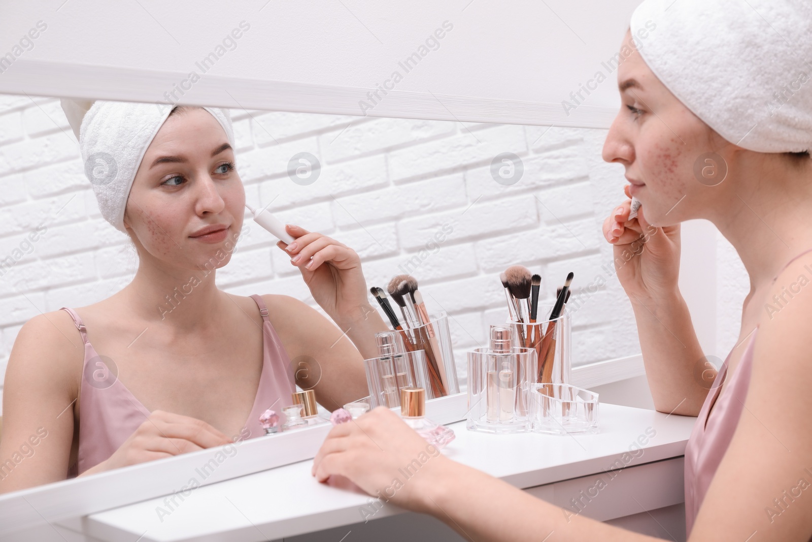 Photo of Woman with acne problem applying cream near mirror indoors