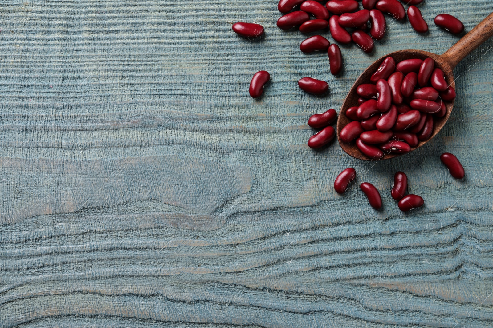 Photo of Raw red kidney beans with spoon on light blue wooden table, flat lay. Space for text
