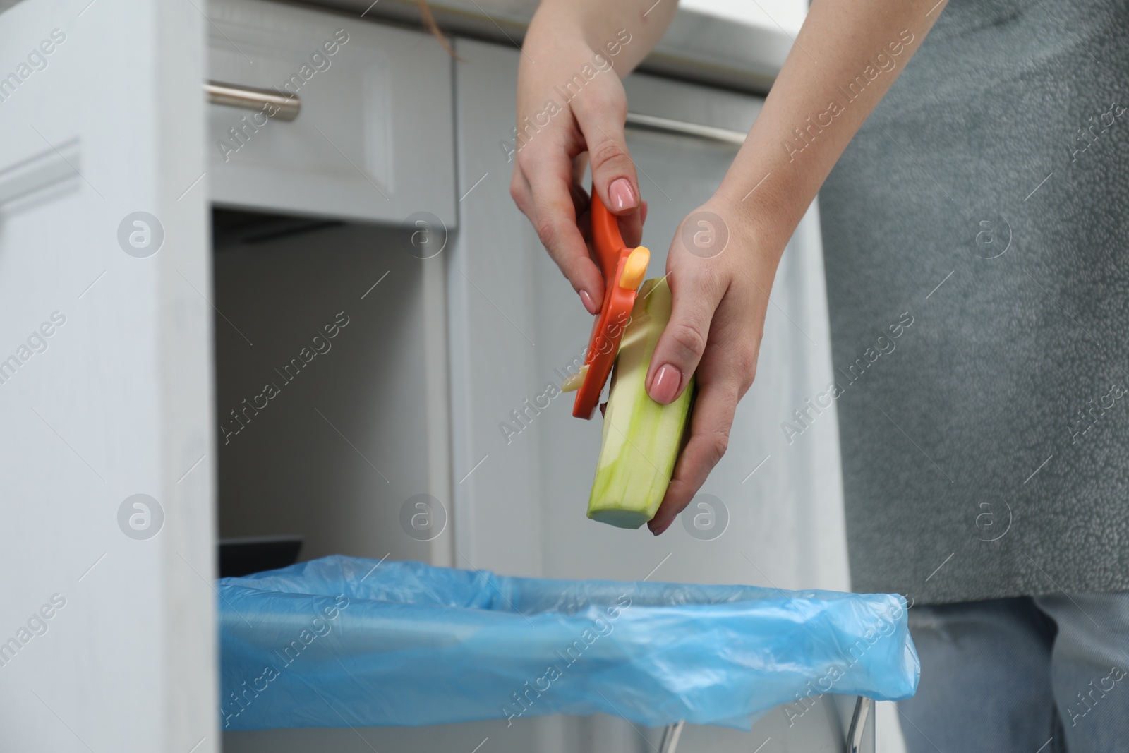 Photo of Woman peeling fresh zucchini above garbage bin indoors, closeup