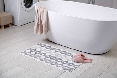 Photo of Stylish mat and slippers on floor near tub in bathroom. Interior design