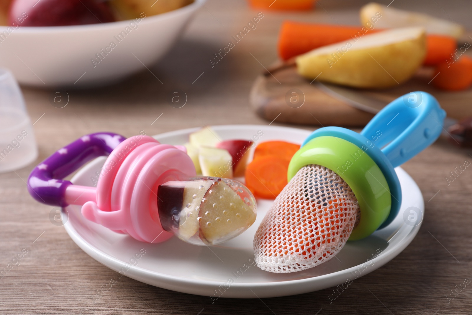 Photo of Different nibblers with fresh apple and boiled carrot on wooden table, closeup. Baby feeder