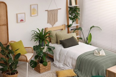 Large comfortable bed and potted houseplants in stylish bedroom. Interior design