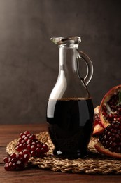 Photo of Glass jug of tasty pomegranate sauce and fresh ripe fruit on wooden table