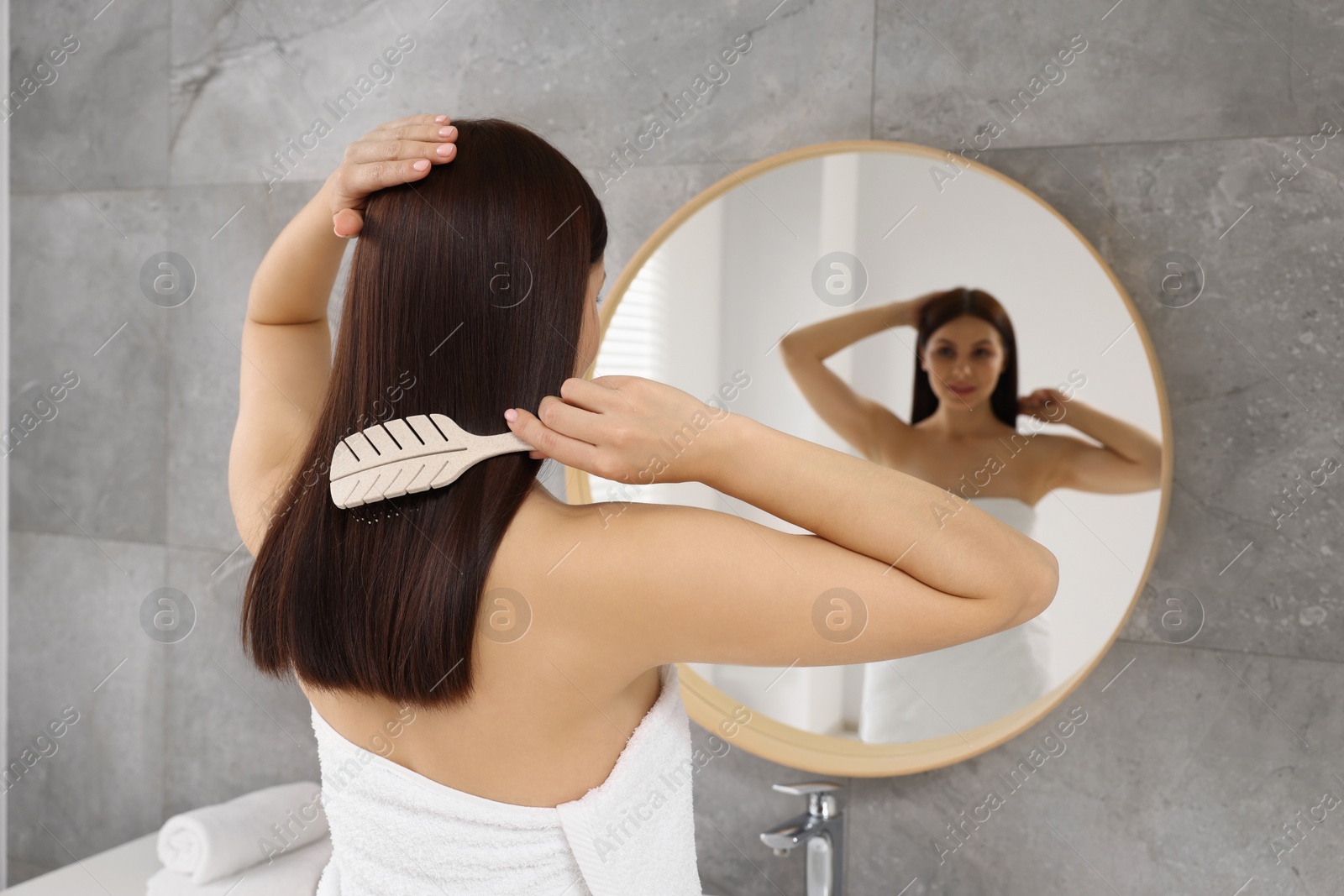 Photo of Beautiful woman brushing her hair near mirror in bathroom