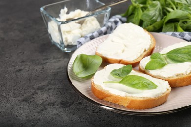 Photo of Delicious sandwiches with cream cheese and basil leaves on grey table. Space for text