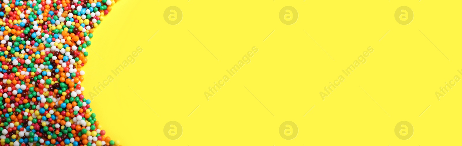 Photo of Bright colorful sprinkles on yellow background, flat lay with space for text. Confectionery decor