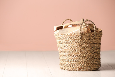 Wicker basket with cut firewood on white floor indoors. Space for text