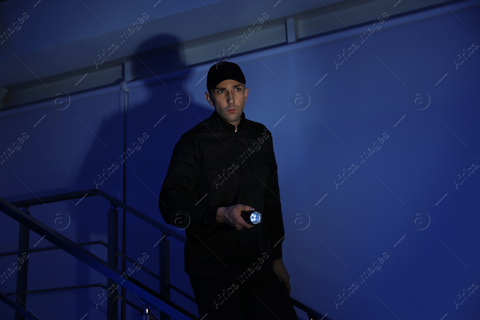 Photo of Male security guard with flashlight on stairs in darkness