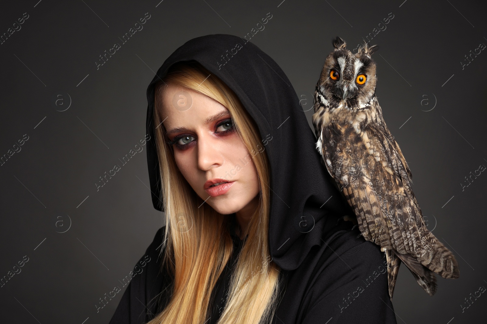 Photo of Witch in black mantle with owl on dark background. Scary fantasy character