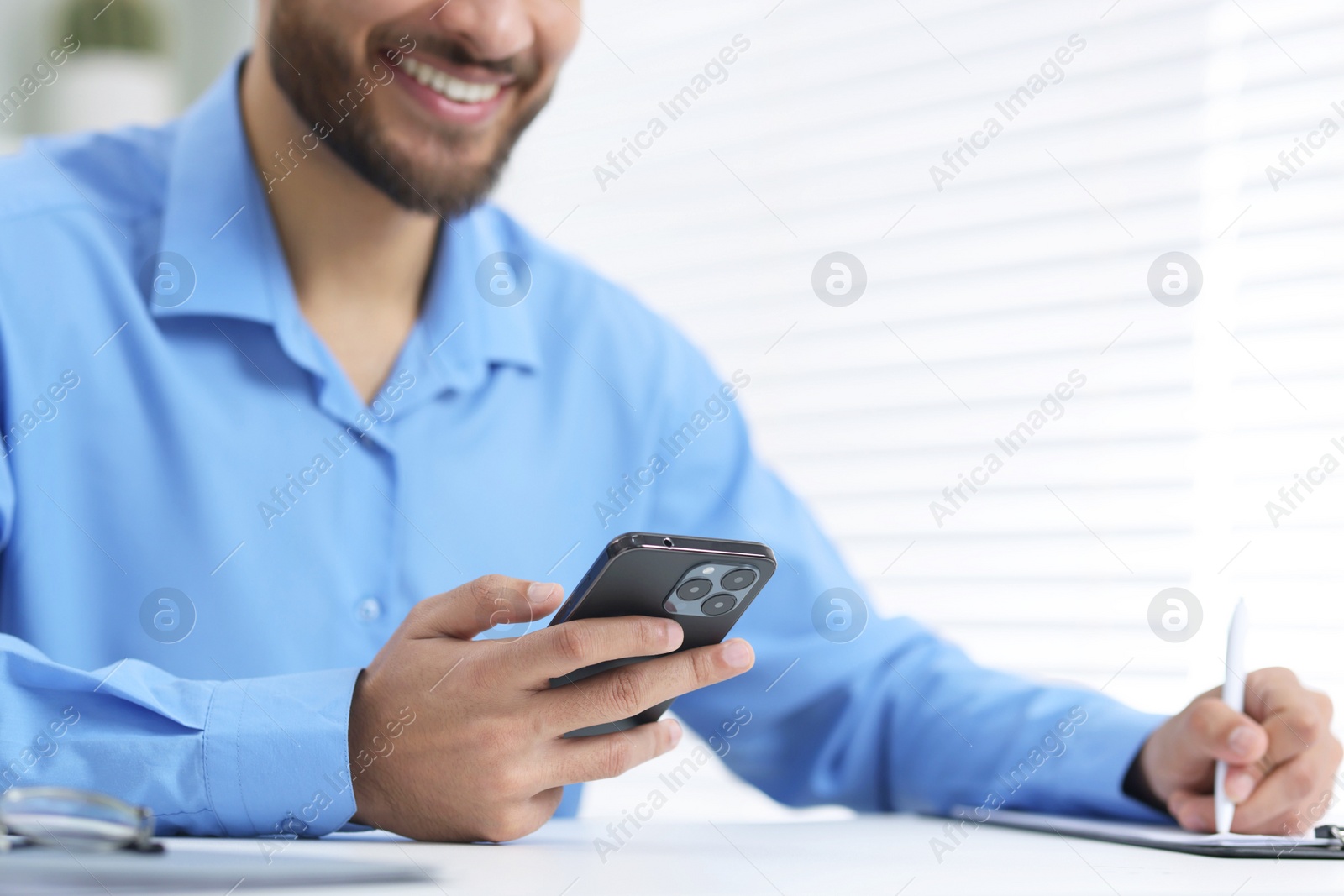 Photo of Man using smartphone while working at white table in office, closeup