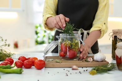 Woman putting rosemary into pickling jar at kitchen table, closeup