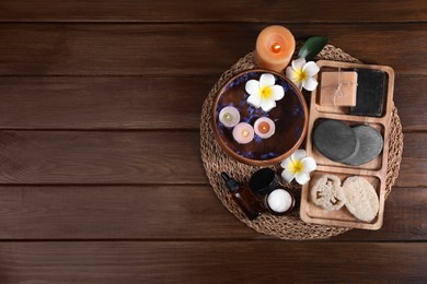 Different spa products, plumeria flowers and burning candles on wooden table, top view. Space for text