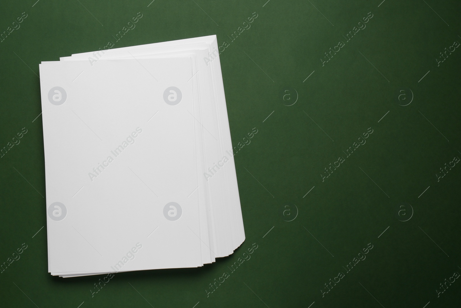 Photo of White paper sheets on dark green background, top view. Space for text