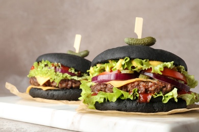 Photo of Board with black burgers on table against color background, closeup