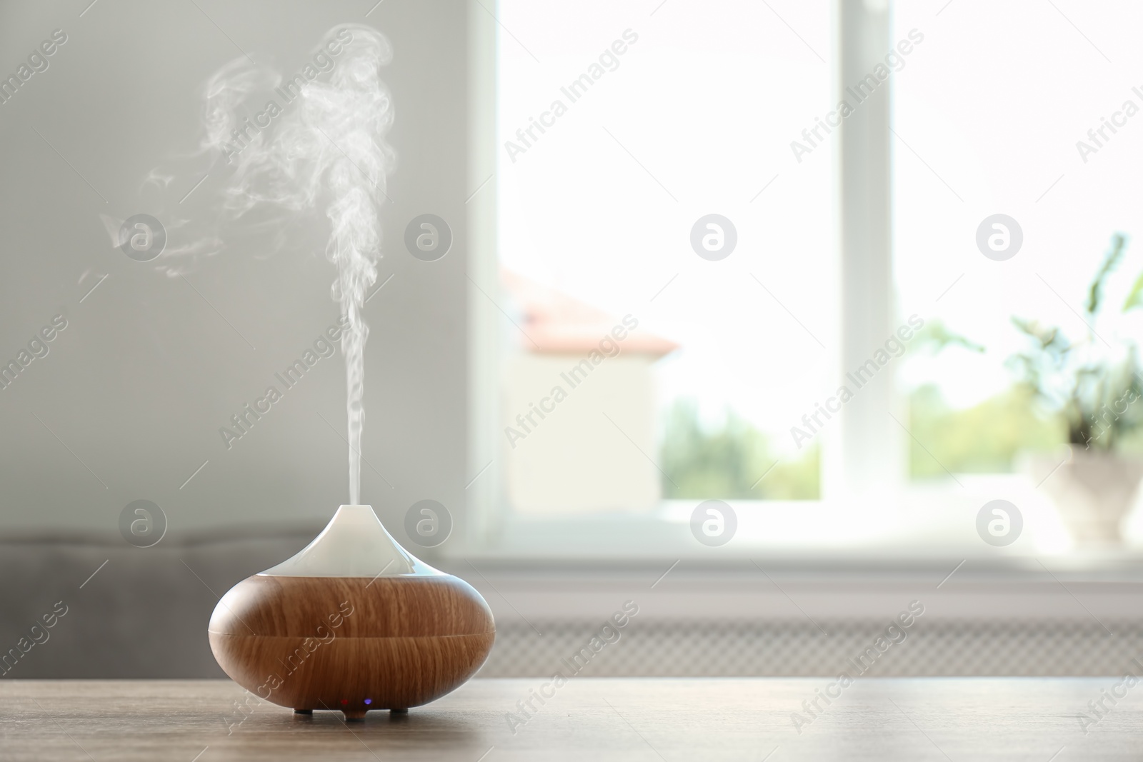 Photo of Modern aroma lamp on table against blurred background with space for text