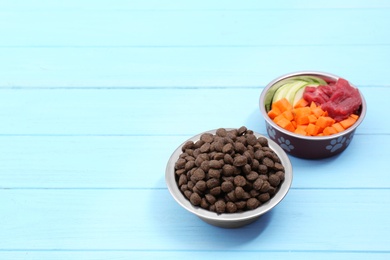 Photo of Bowls with dry and natural dog food on wooden background. Space for text