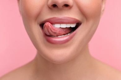 Woman with beautiful lips licking her teeth on pink background, closeup