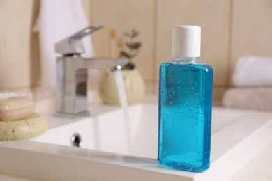 Photo of Fresh mouthwash in bottle on sink in bathroom, closeup. Space for text
