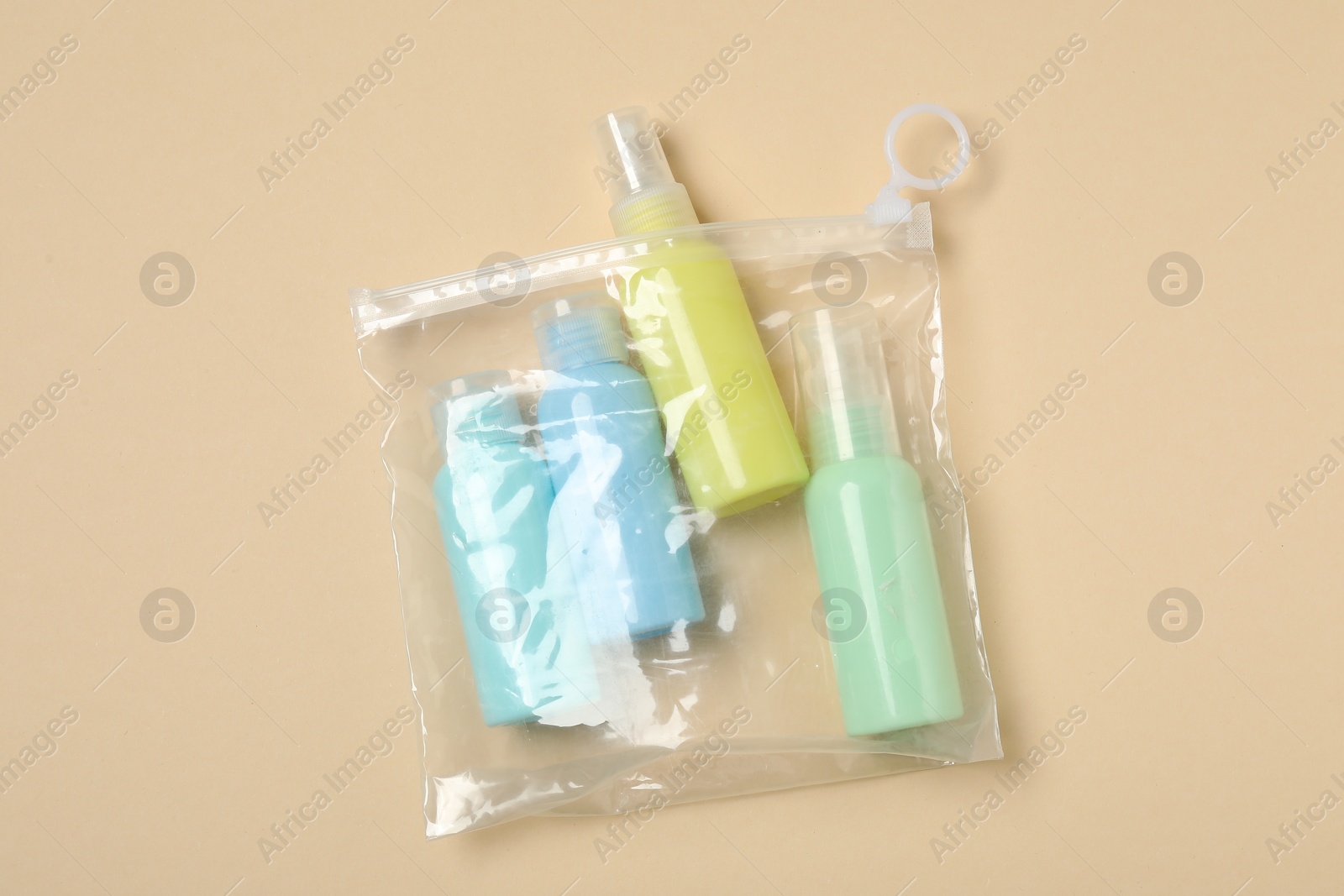 Photo of Cosmetic travel kit in plastic bag on beige background, top view. Bath accessories