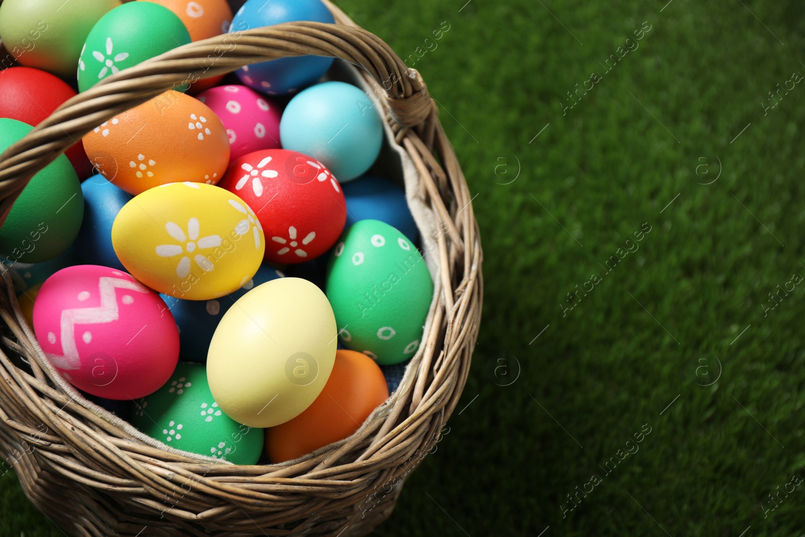 Photo of Colorful Easter eggs in basket on green grass, closeup. Space for text