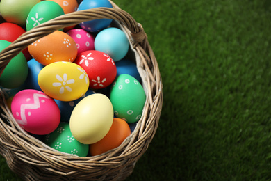 Colorful Easter eggs in basket on green grass, closeup. Space for text