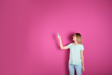 Photo of Woman with air conditioner remote on color background