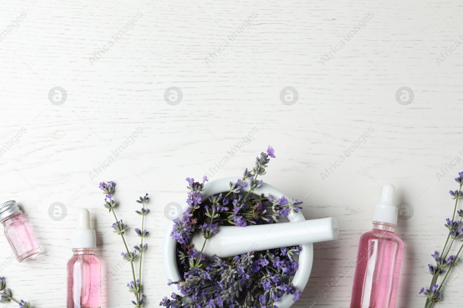 Photo of Bottles of essential oil, mortar and pestle with lavender flowers on white wooden background, flat lay. Space for text