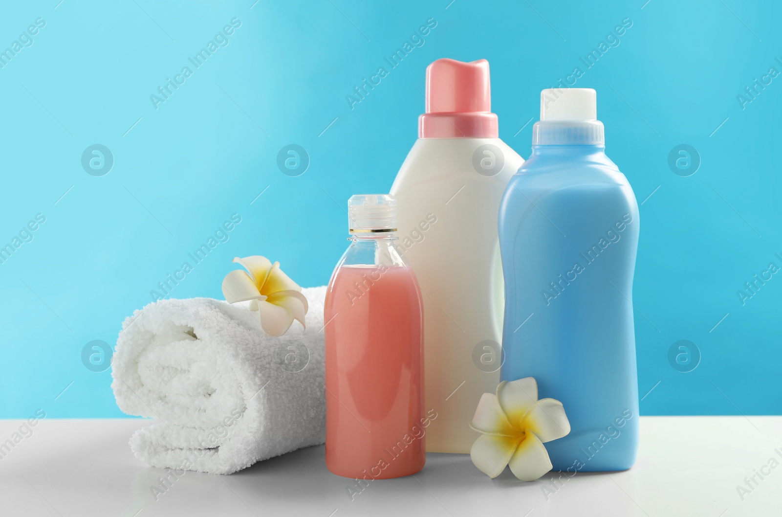 Photo of Bottles of laundry detergents, towel and plumeria flowers on white table