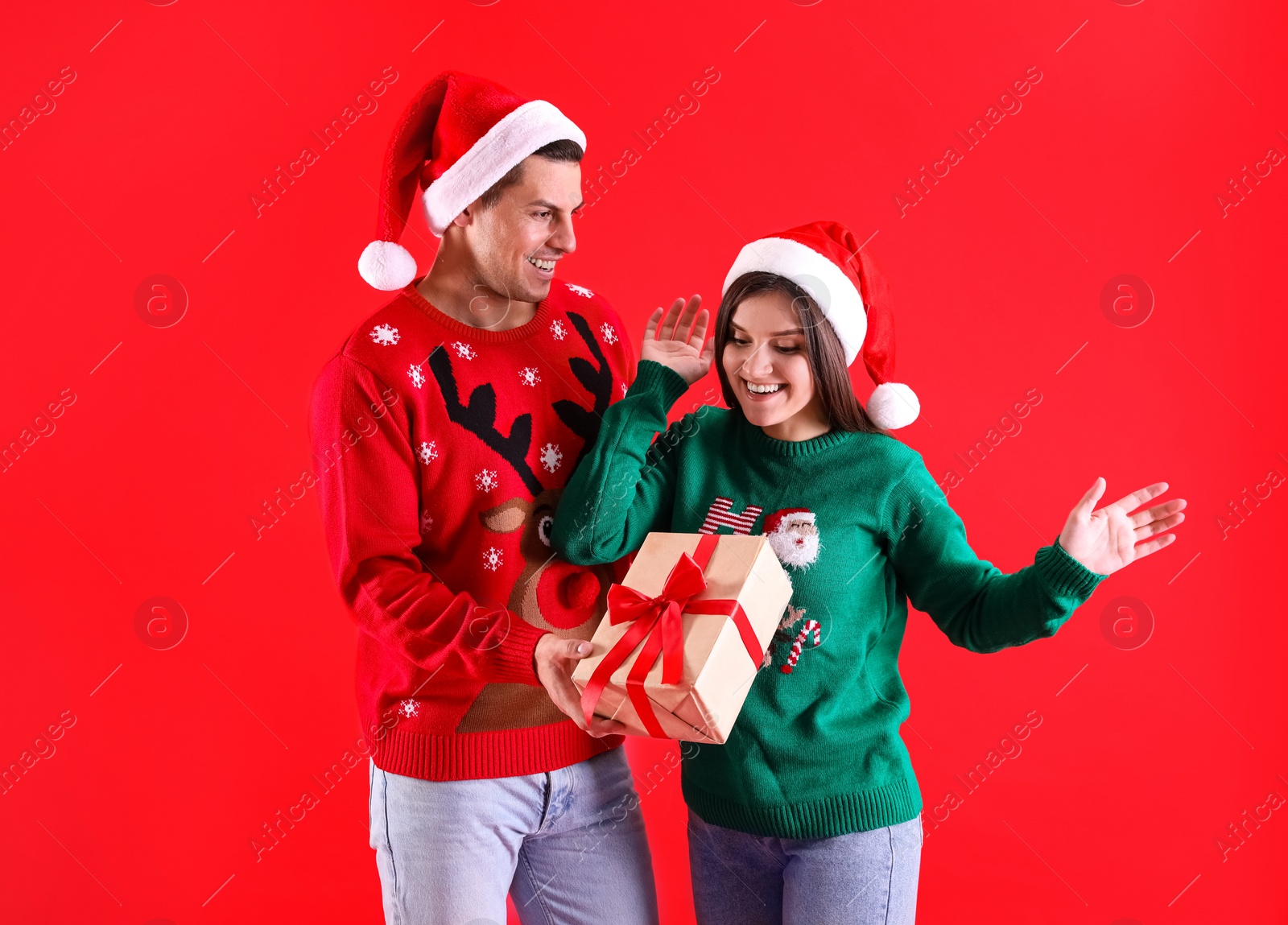 Photo of Man presenting Christmas gift to his girlfriend on red background