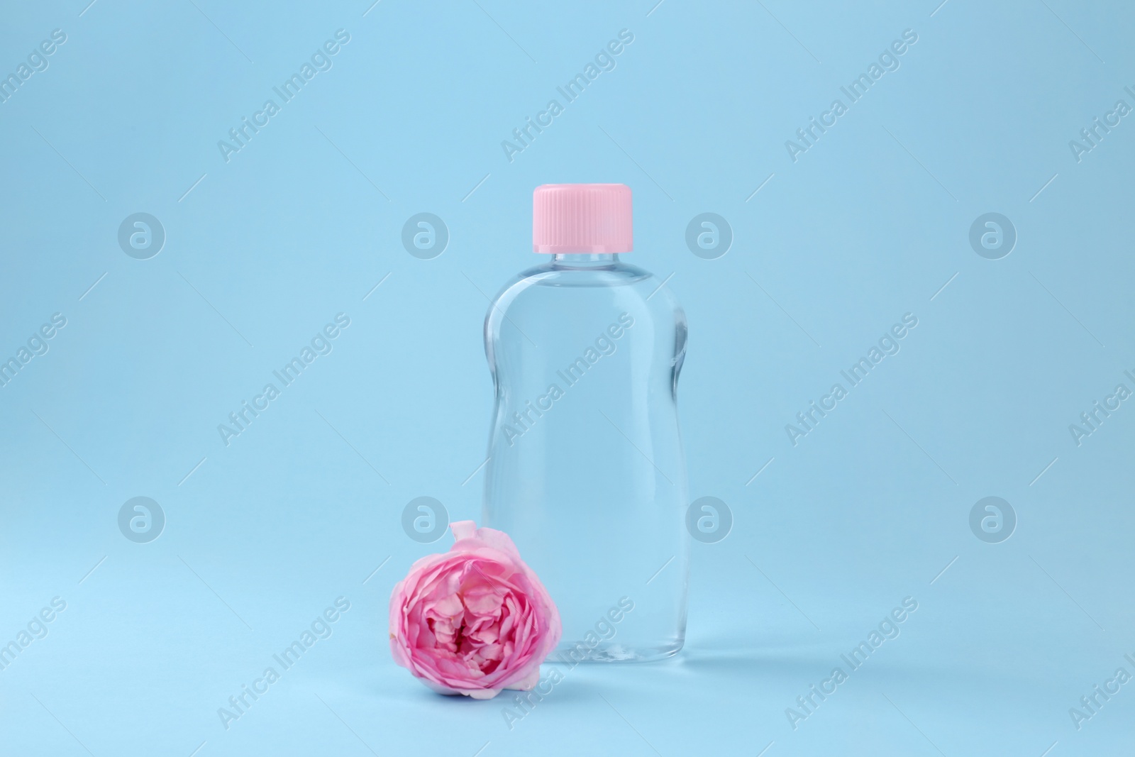 Photo of Bottle with baby oil and beautiful flower on light blue background. Space for text