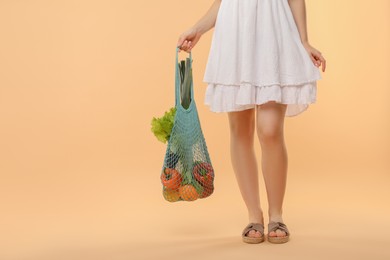 Photo of Woman with string bag of fresh vegetables on beige background, closeup. Space for text