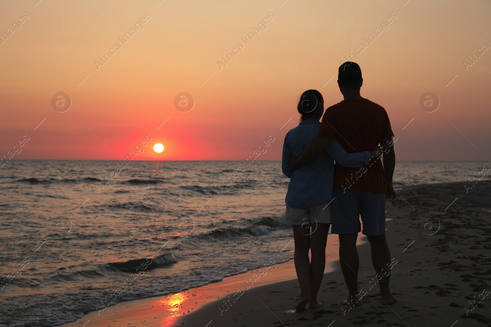 Photo of Couple spending time together on beach at sunset, back view