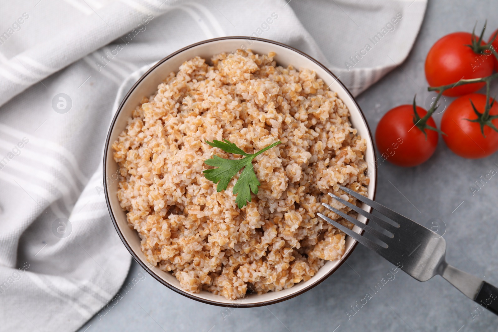 Photo of Tasty wheat porridge with parsley and tomatoes in bowl on grey table, flat lay