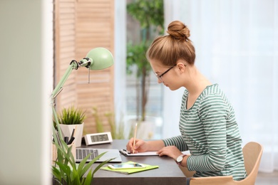 Pretty teenage girl doing homework at table in room