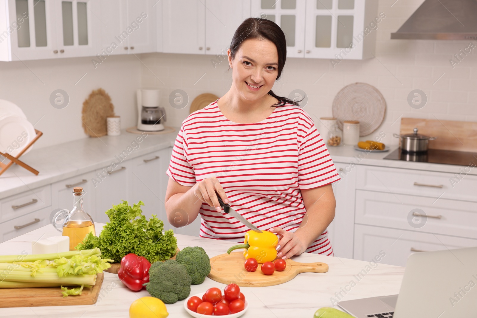 Photo of Beautiful overweight woman preparing healthy meal at table in kitchen