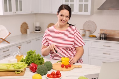 Photo of Beautiful overweight woman preparing healthy meal at table in kitchen