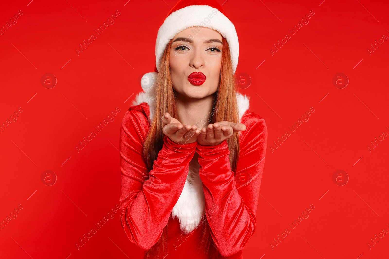 Photo of Young woman in Santa hat blowing kiss on red background. Christmas celebration