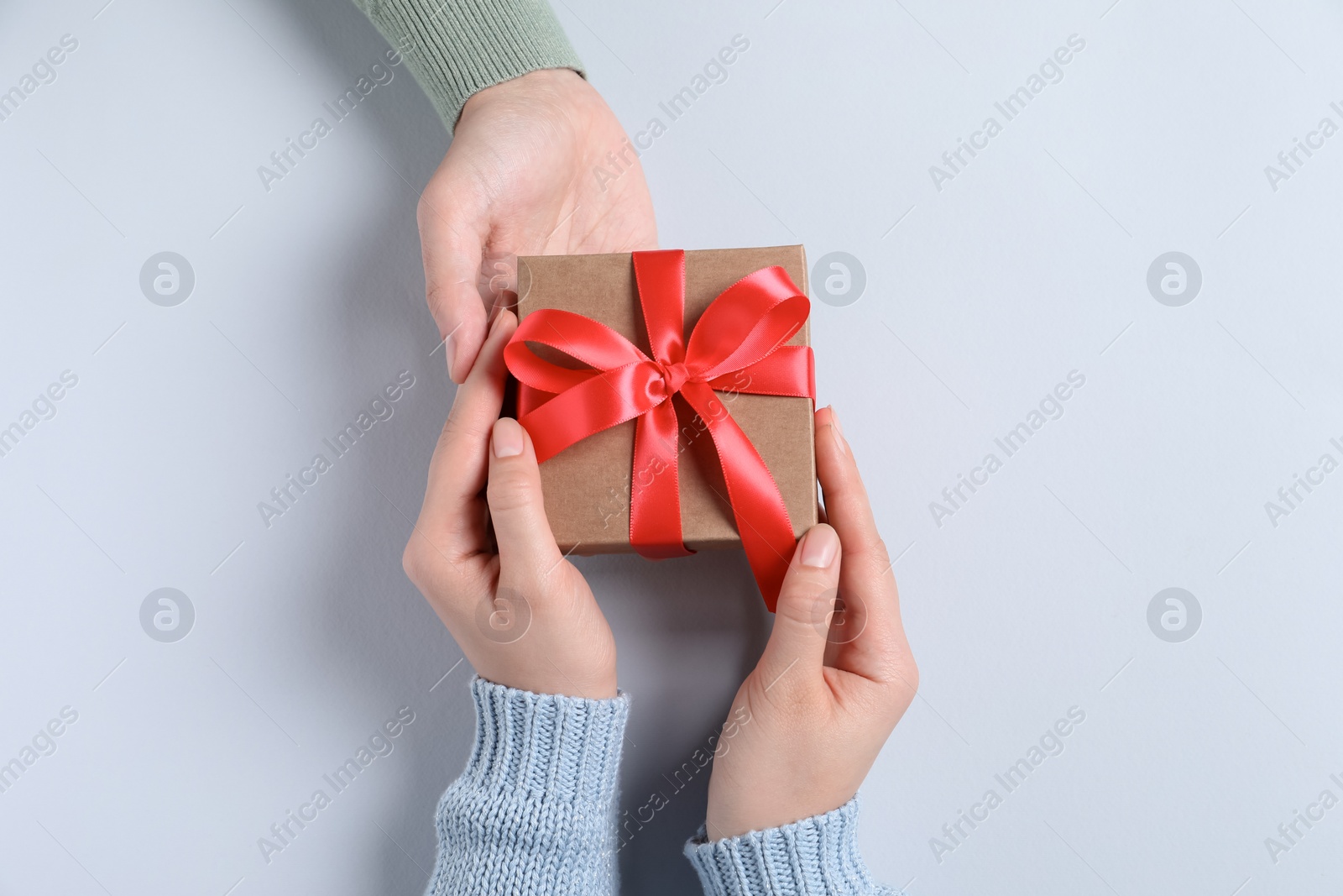 Photo of Man giving gift box to woman on light gray background, top view