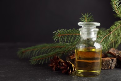 Photo of Pine essential oil, cones and branches on black table, closeup. Space for text