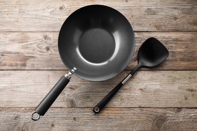 Black metal wok and spatula on wooden table, top view