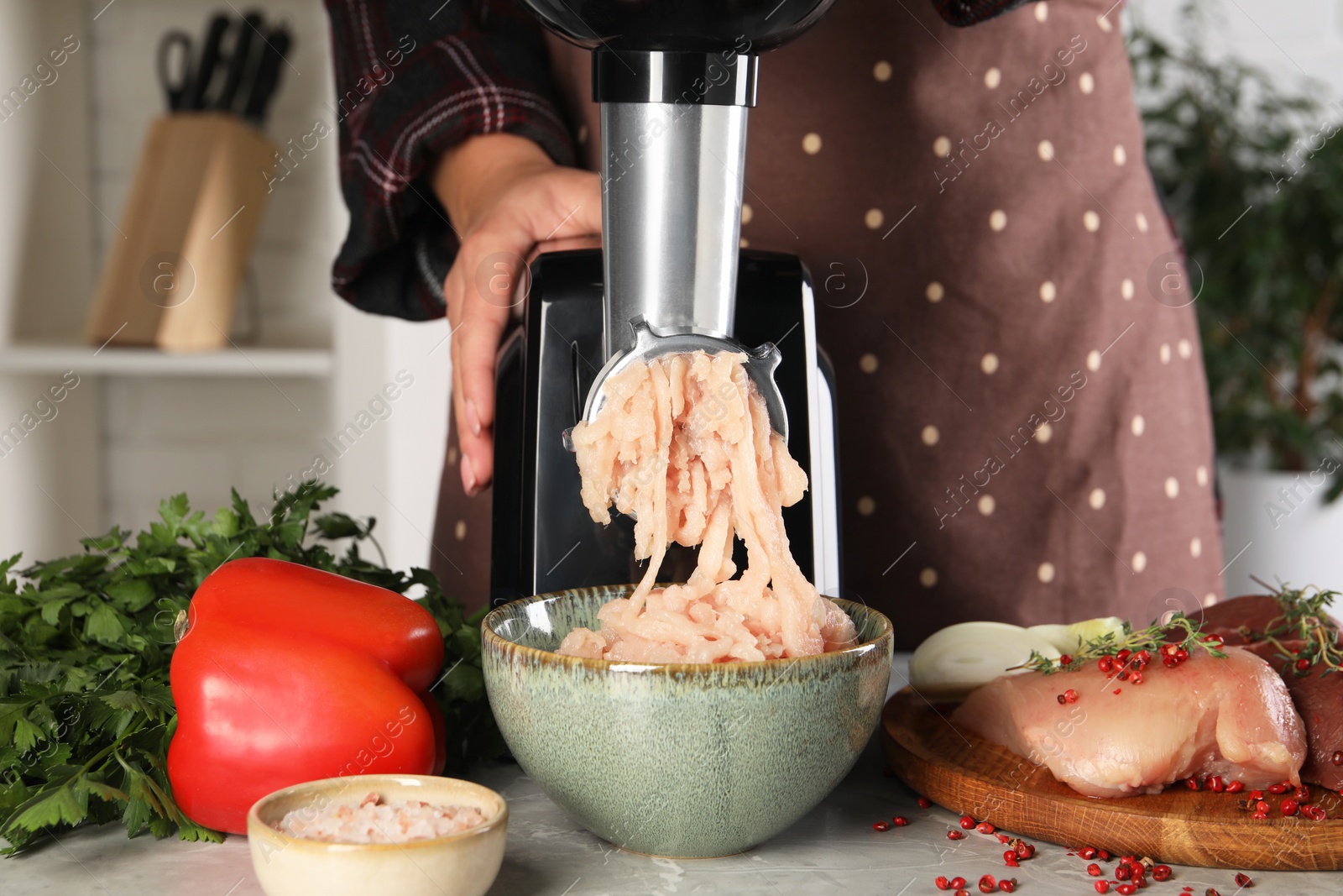 Photo of Woman making chicken mince with electric meat grinder at grey marble table indoors, closeup