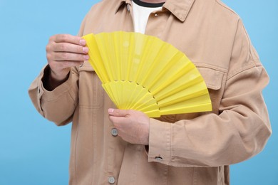 Man holding hand fan on light blue background, closeup