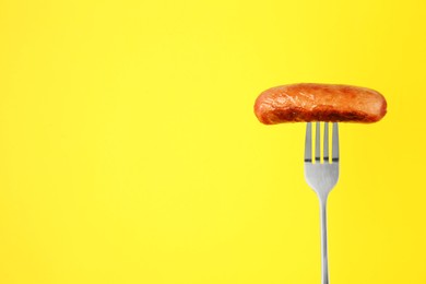 Fork with tasty fried sausage on yellow background. Space for text