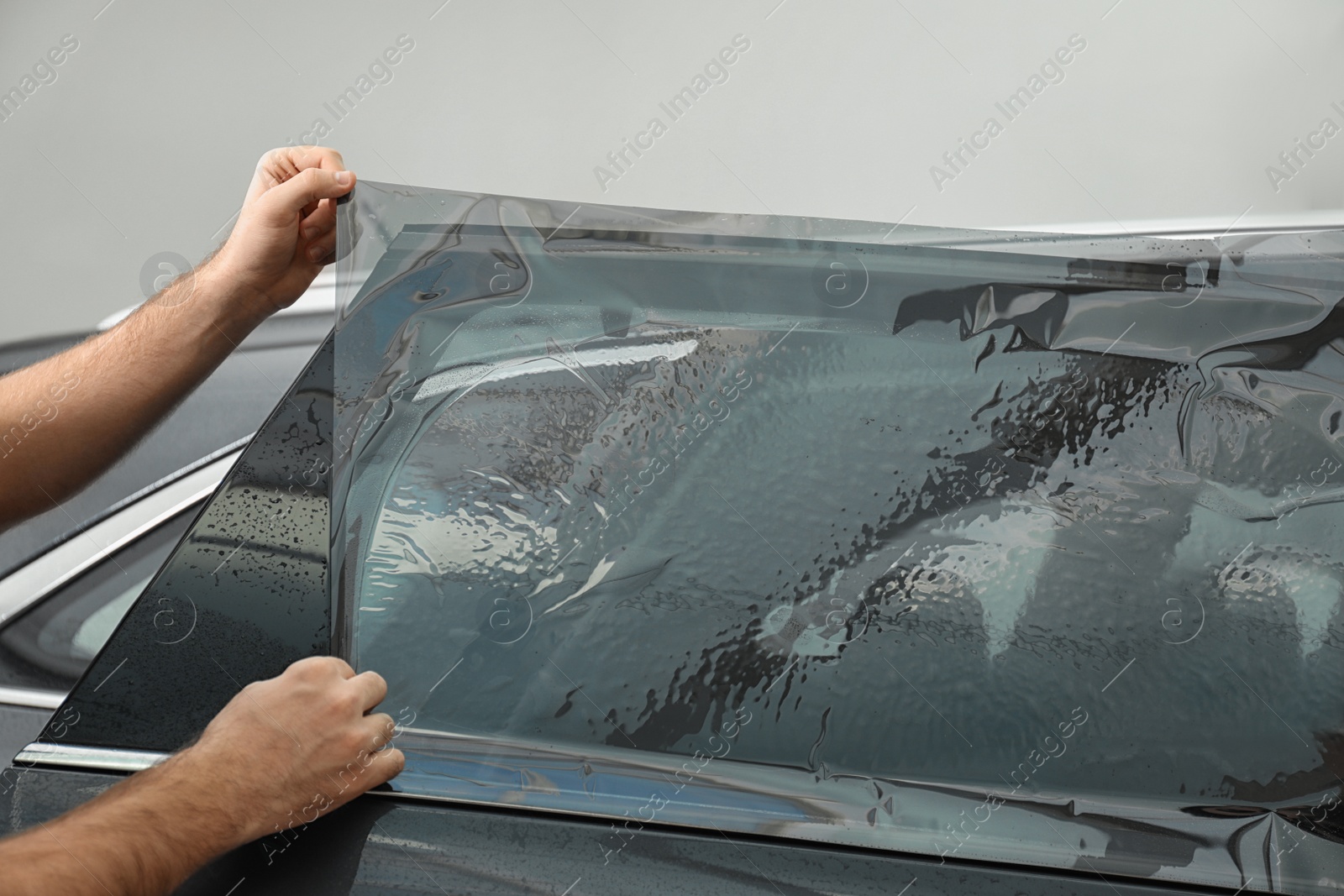 Photo of Worker tinting car window with foil in workshop, closeup