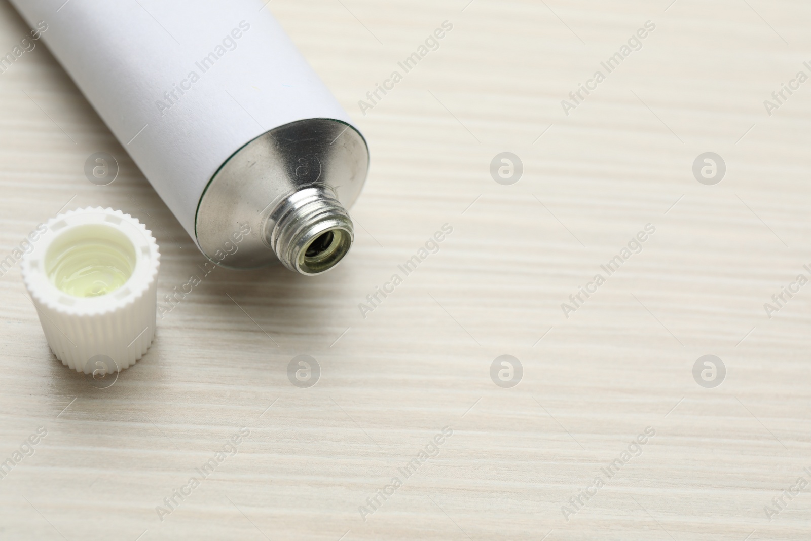 Photo of Open white tube of ointment on light wooden table, closeup. Space for text