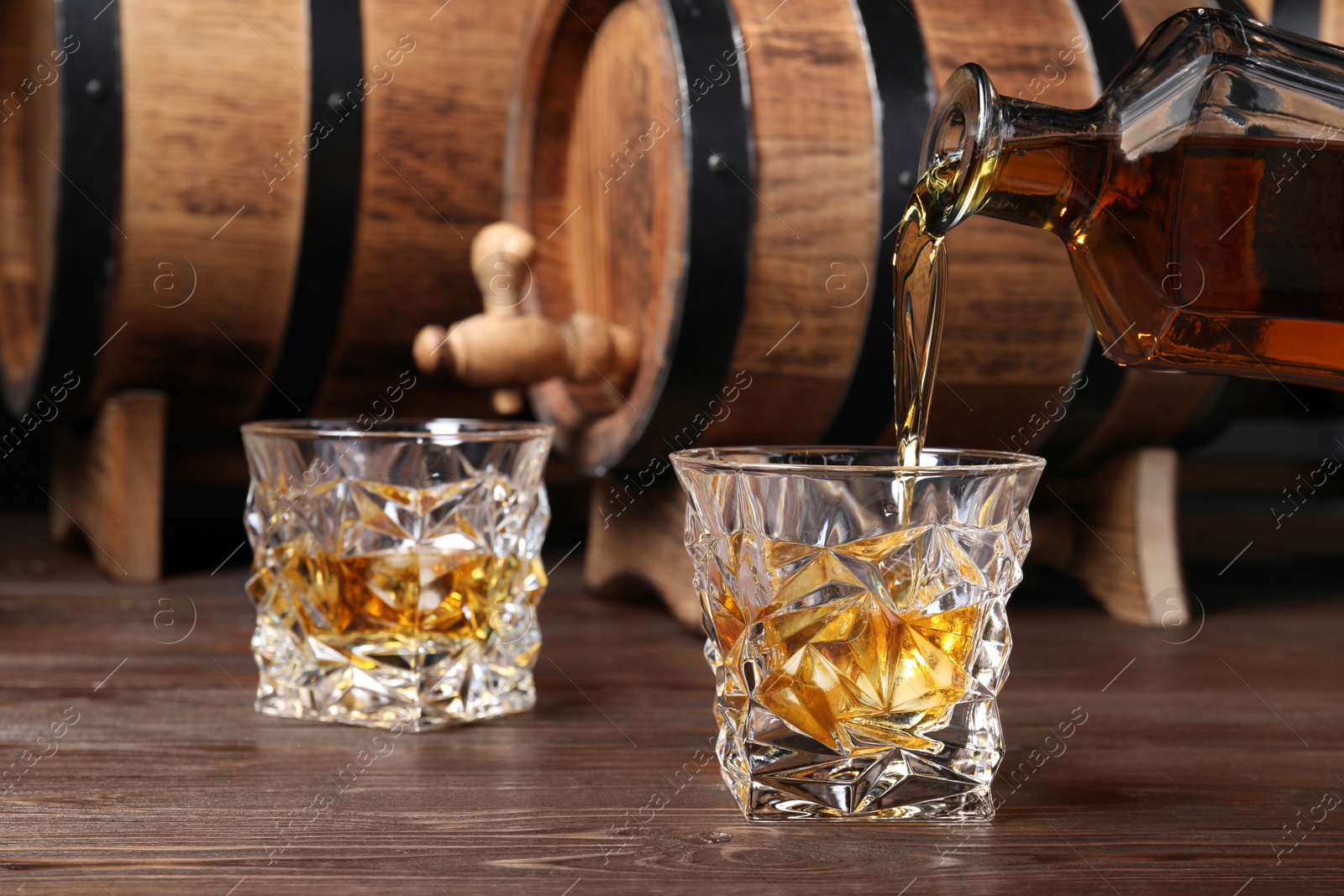 Photo of Pouring whiskey from bottle into glass on wooden table