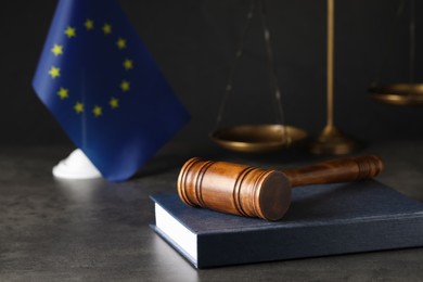 Photo of Wooden judge's gavel and book on grey table near European Union flag. Space for text